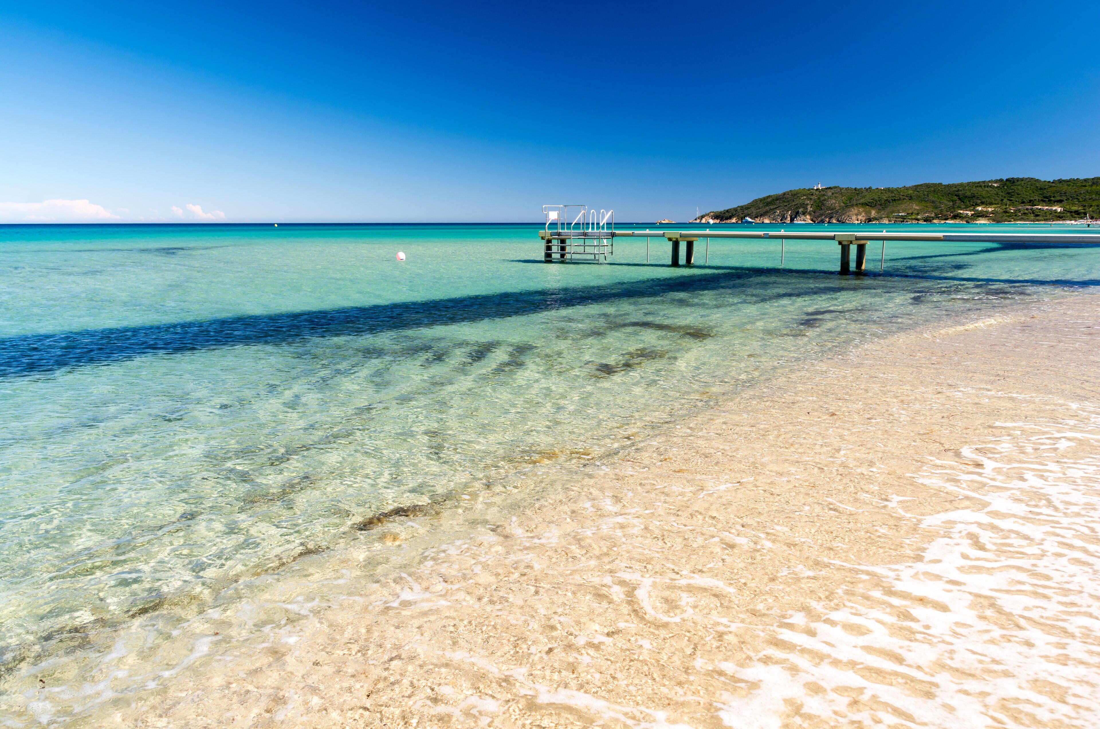 Crystal water and sand at Plage de Pampelonne, with a wooden jetty reaching into a transparent sea